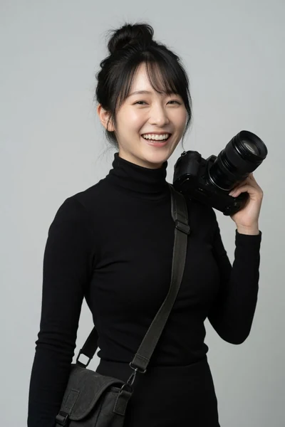 AI-generated Mio, with her hair in a messy bun, wearing a black turtleneck and holding a camera over her shoulder.